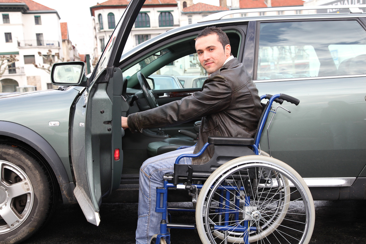 Young man in wheelchair getting in his car