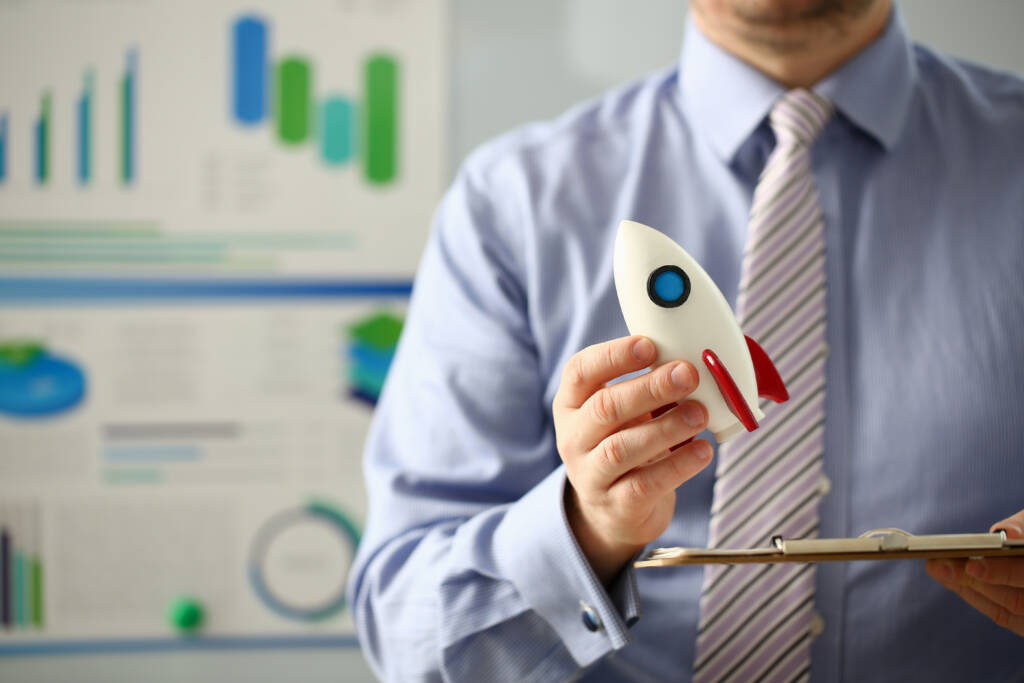 Businessman in suit hold white rocket in hand office background